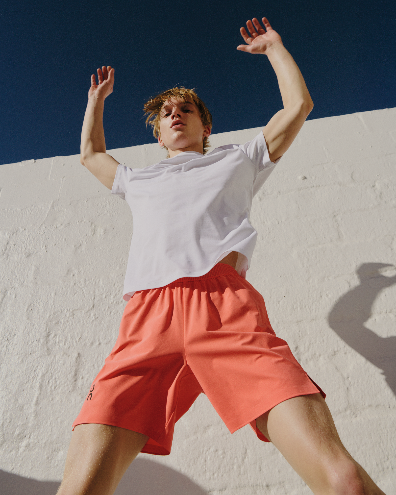 Person outside doing jumping jacks while wearing white On running shoes, white crew socks, and red short.