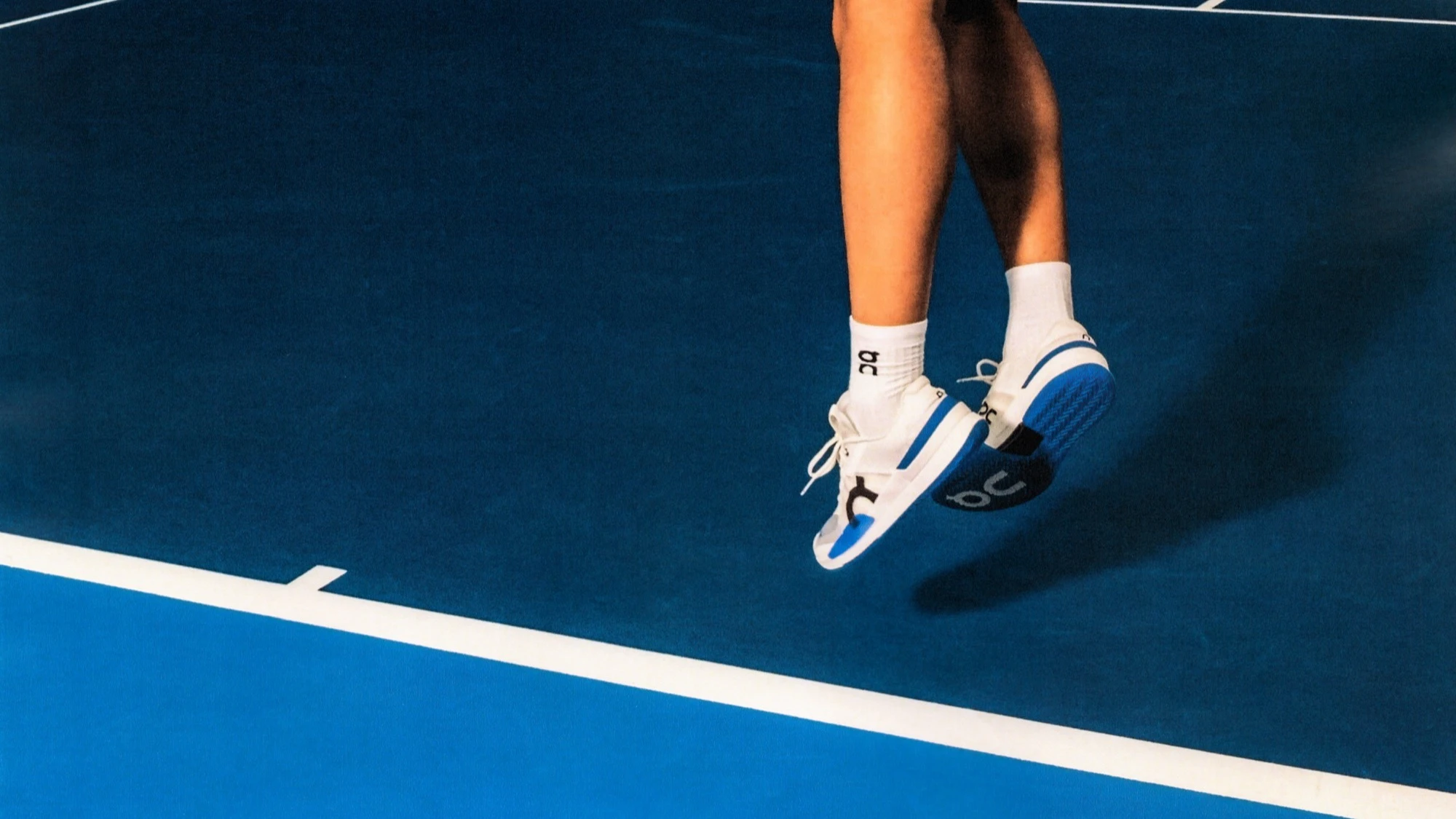 A person jumps near the baseline of a blue tennis court.