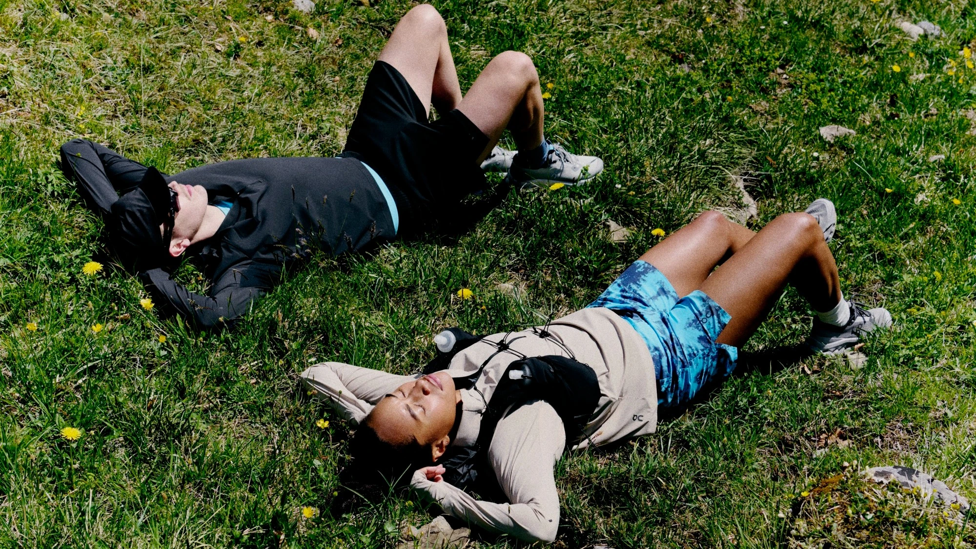 Two runners laying in a grassy field with their eyes closed. 