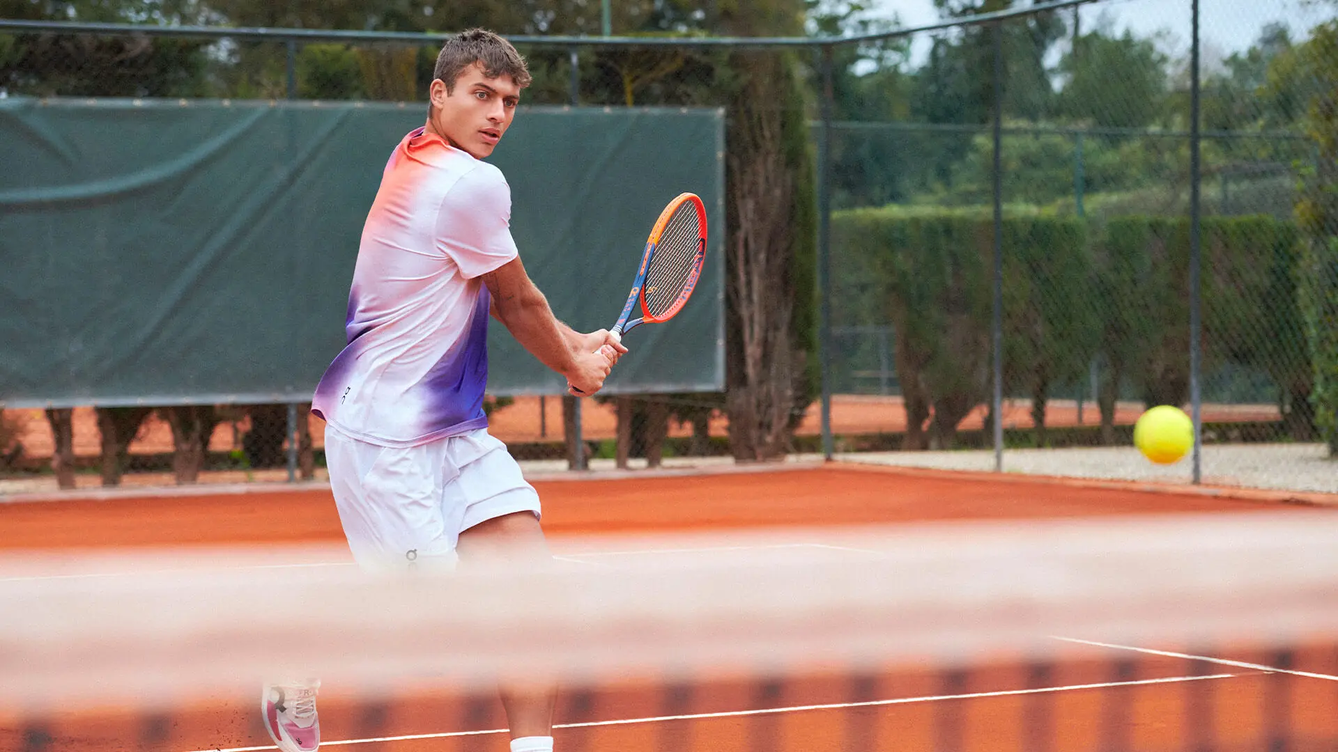 Flavio Cobolli in a multicolored shirt prepares to hit a backhand. 