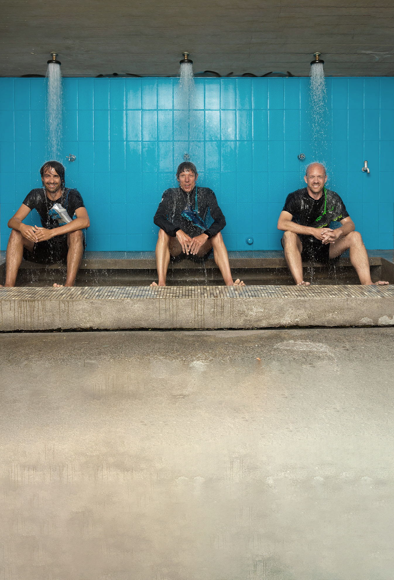 The three On Co-Founders sitting under a blue outdoor shower with water pouring down over them.