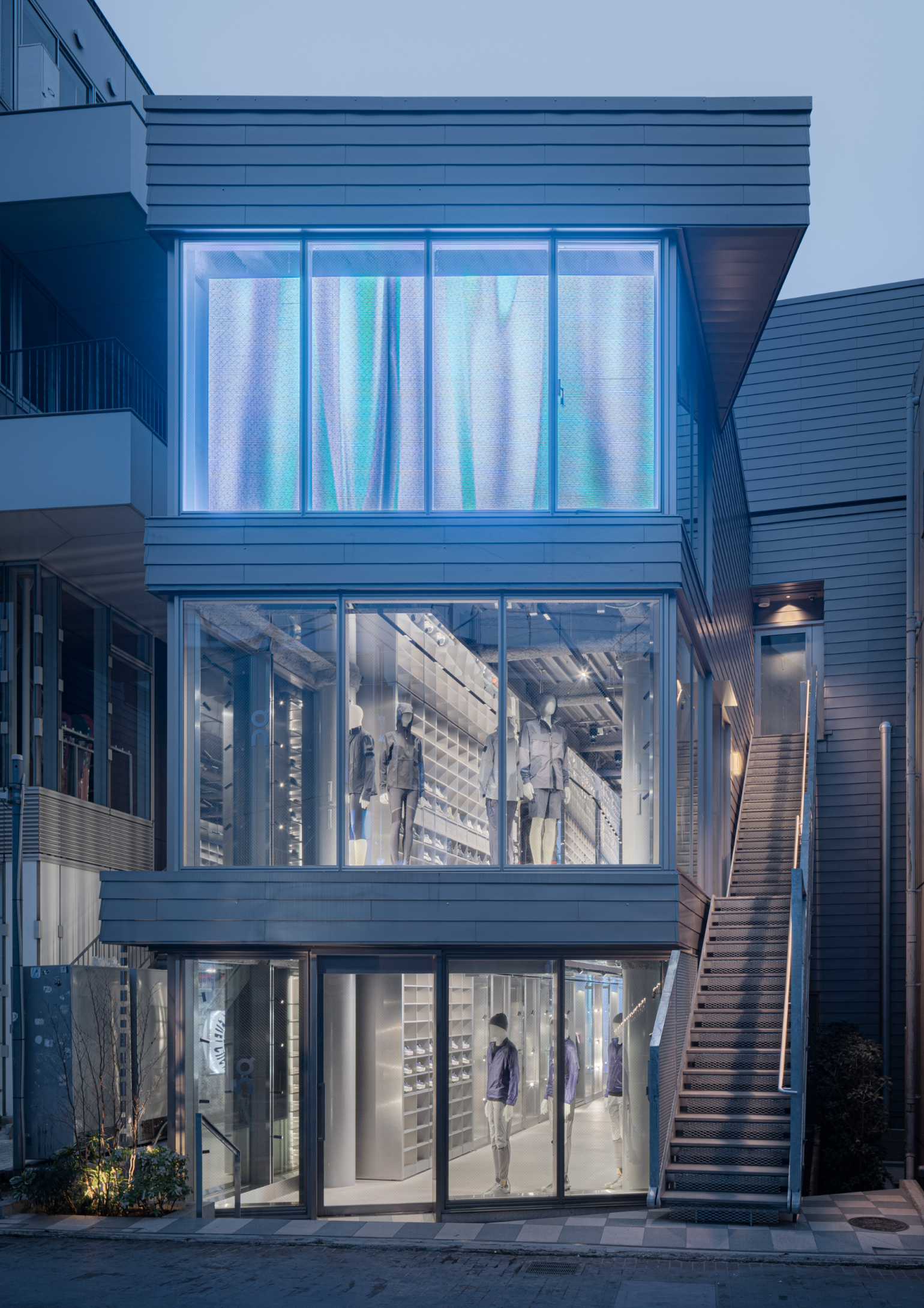 Exterior shot of On store in Tokyo, featuring a glowing neon light amid grey buildings.