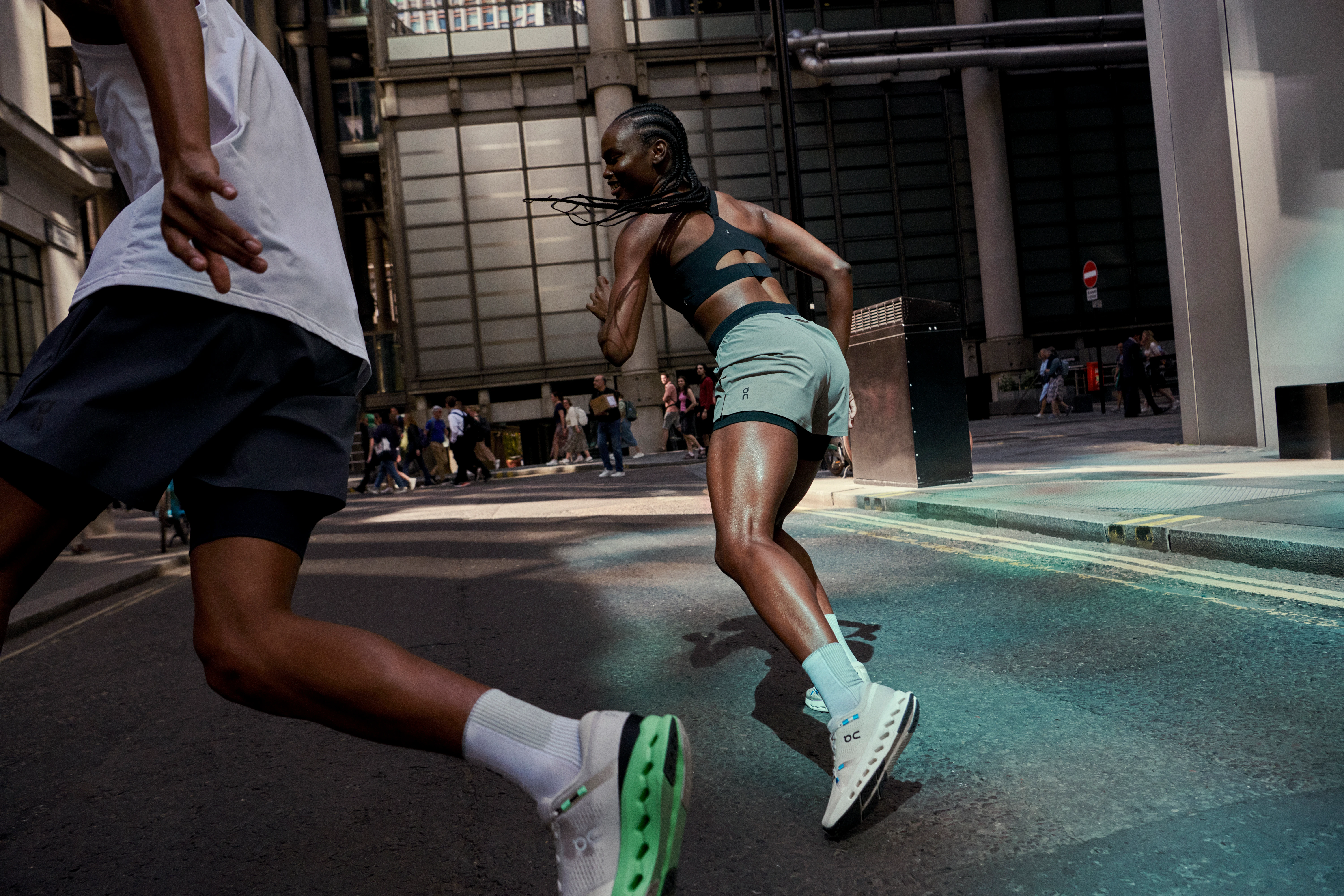 Two athletes sprinting down a city street, both wearing On performance gear.