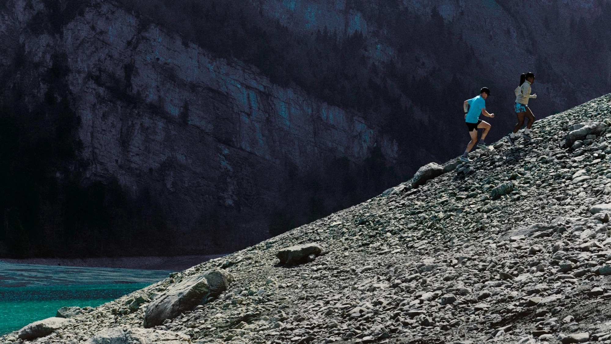 Two runners in the distance, running up a rocky mountainside.
