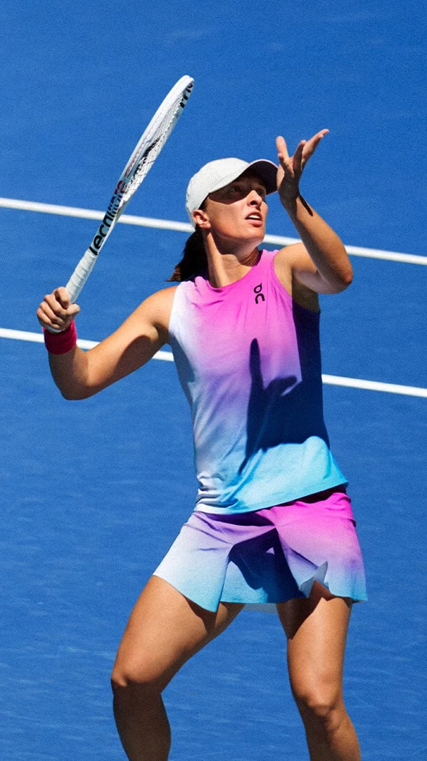 Iga Świątek wearing multi-colored On clothing prepares to serve a tennis ball.