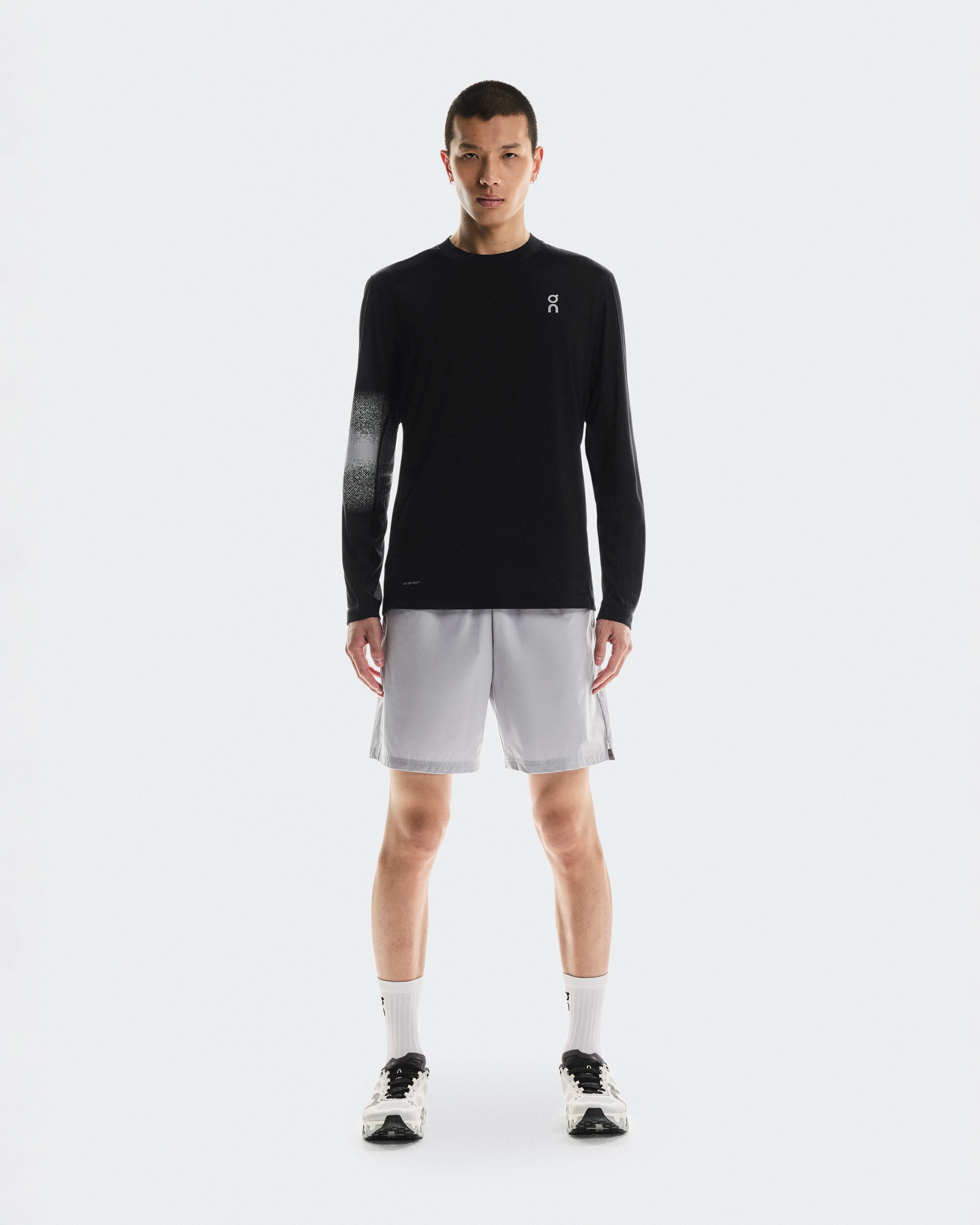 A male athlete standing while wearing an On long-sleeve performance shirt, shorts, and training shoes.