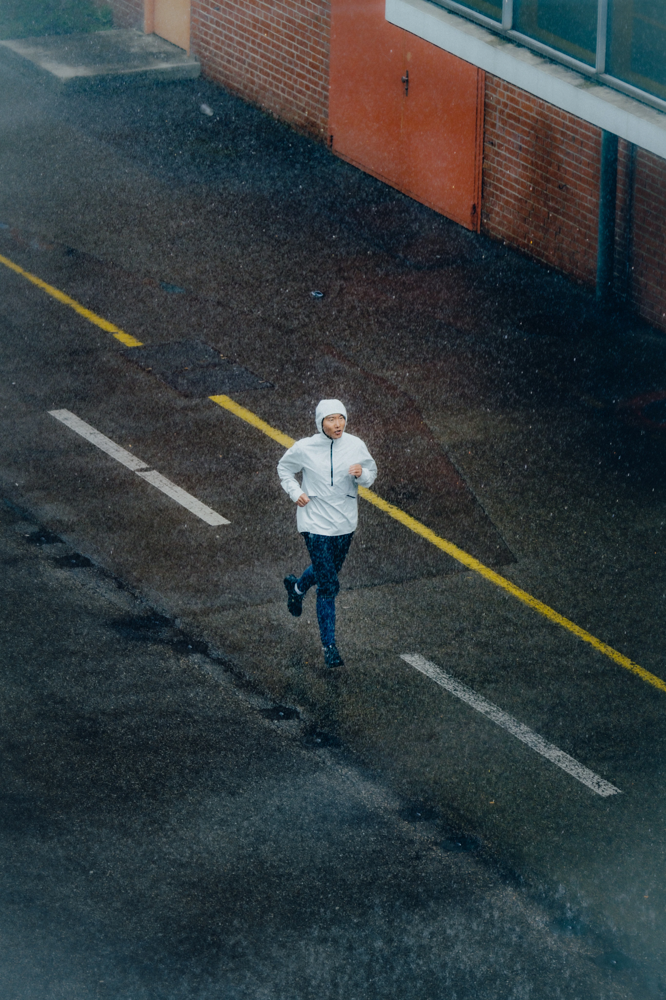 Man running down a road in rainy weather, wearing protective On apparel.
