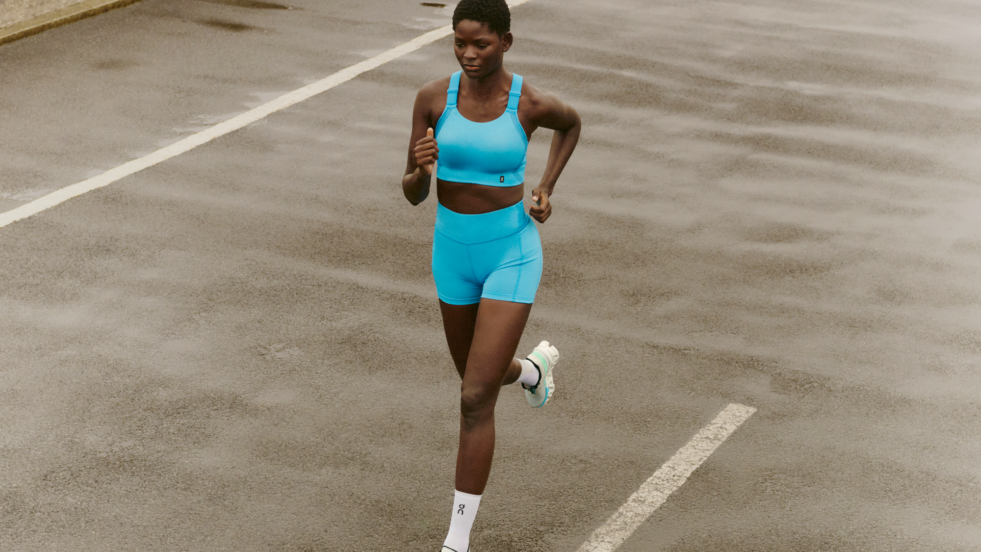 An athletic woman runs on a track in a light blue sports bra and shorts. 
