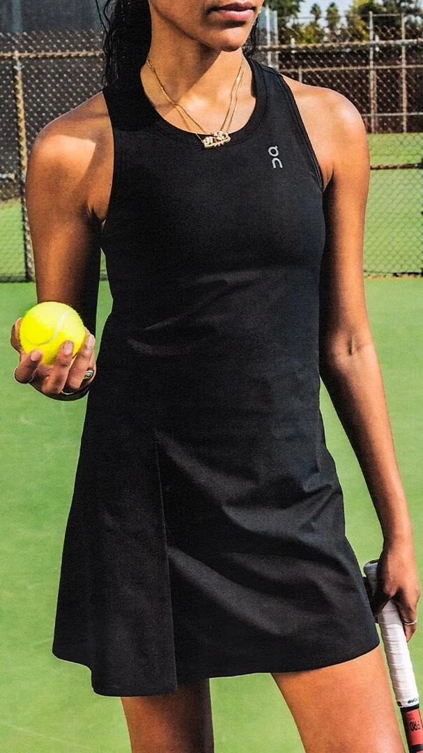 A woman wearing a black mini dress holds a tennis ball and racquet.
