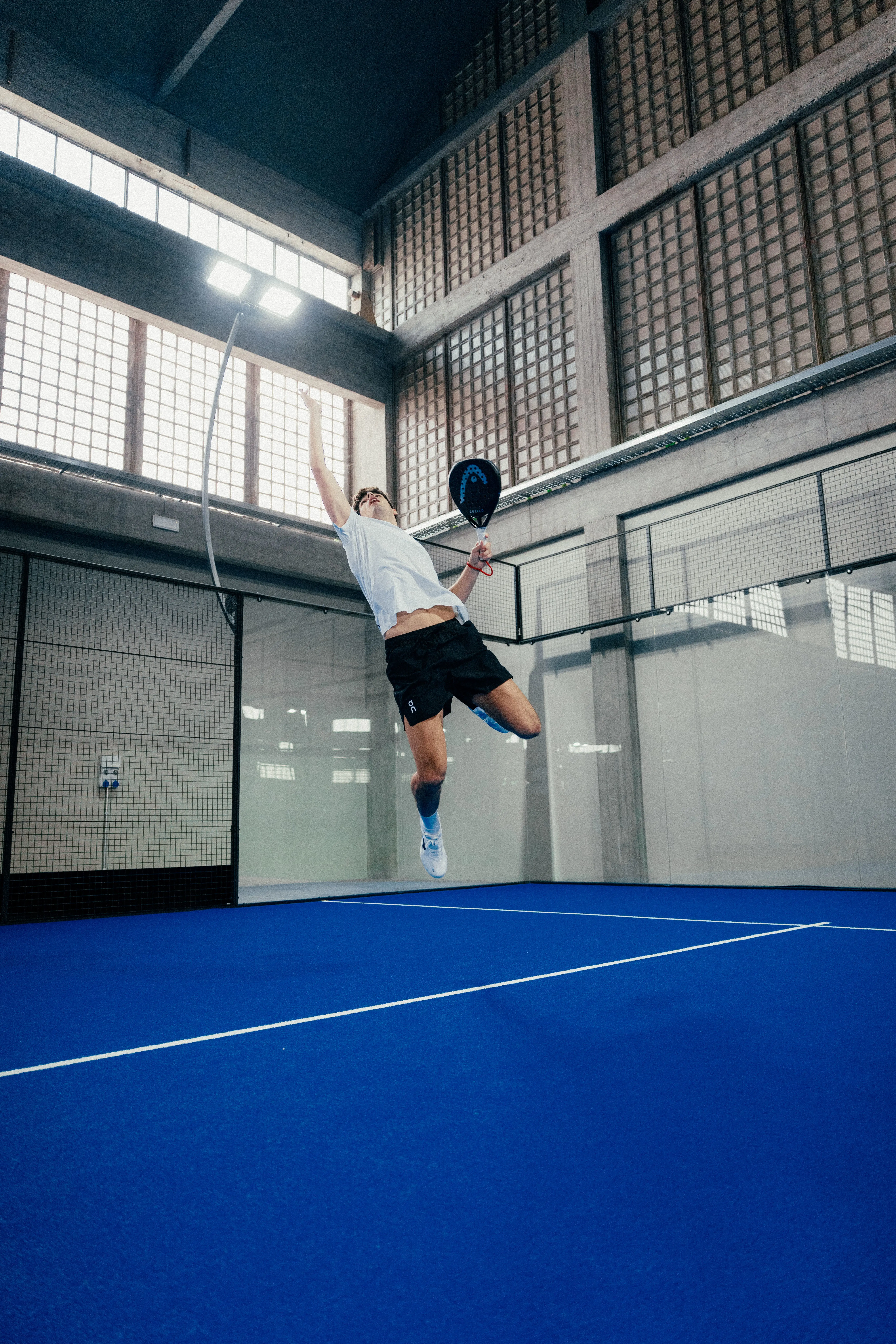 A padel player in full extension, mid-air.