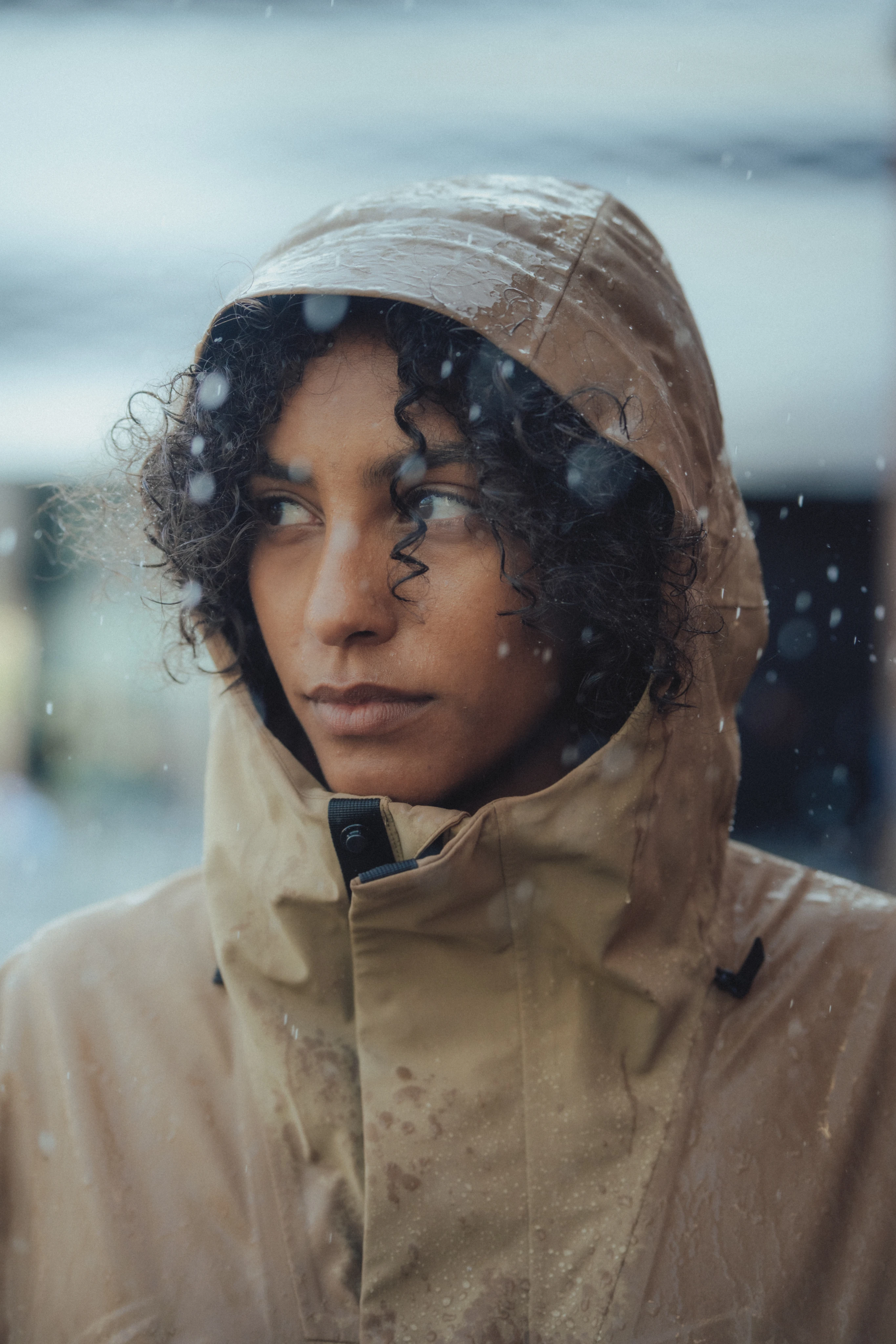 Close-up of a person in the Anorak with the hood up, looking sideways as raindrops fall.