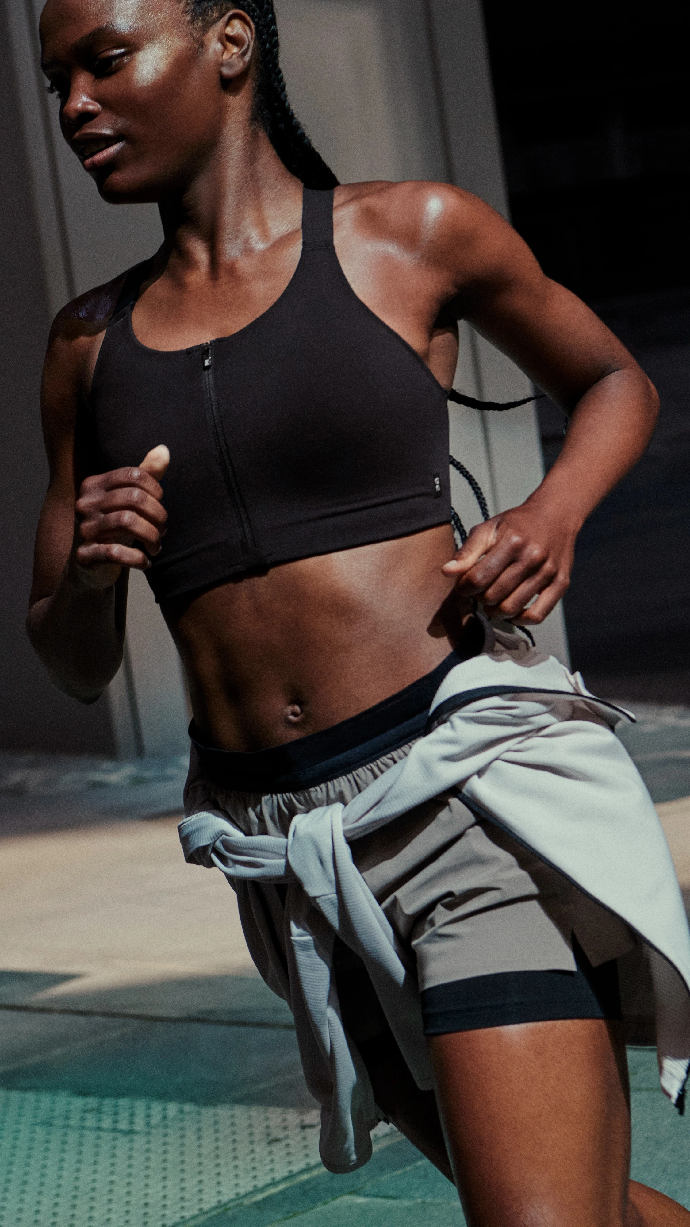 A woman running in a sports bra and shorts with a sweater wrapped around her waist.