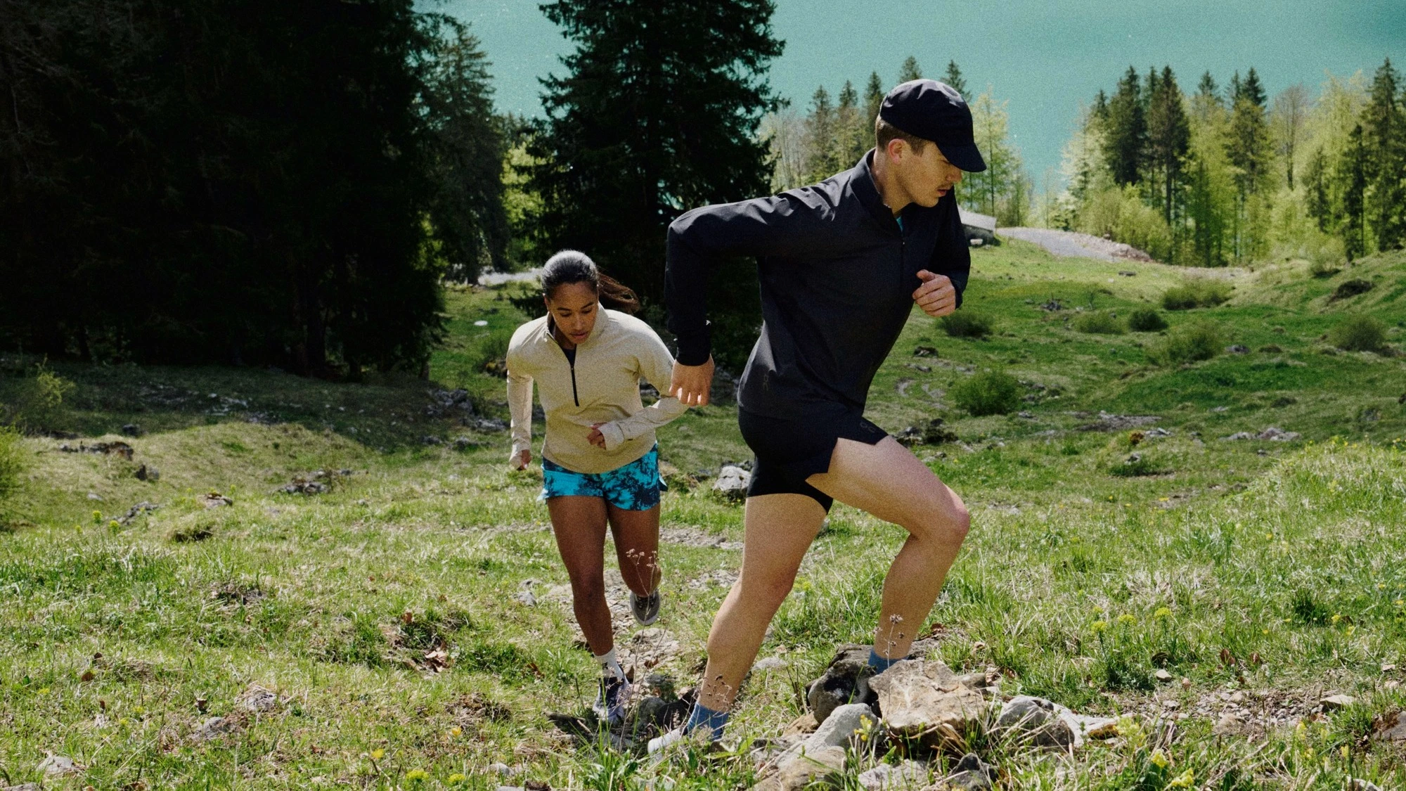 Two runners going up a grassy mountainside.