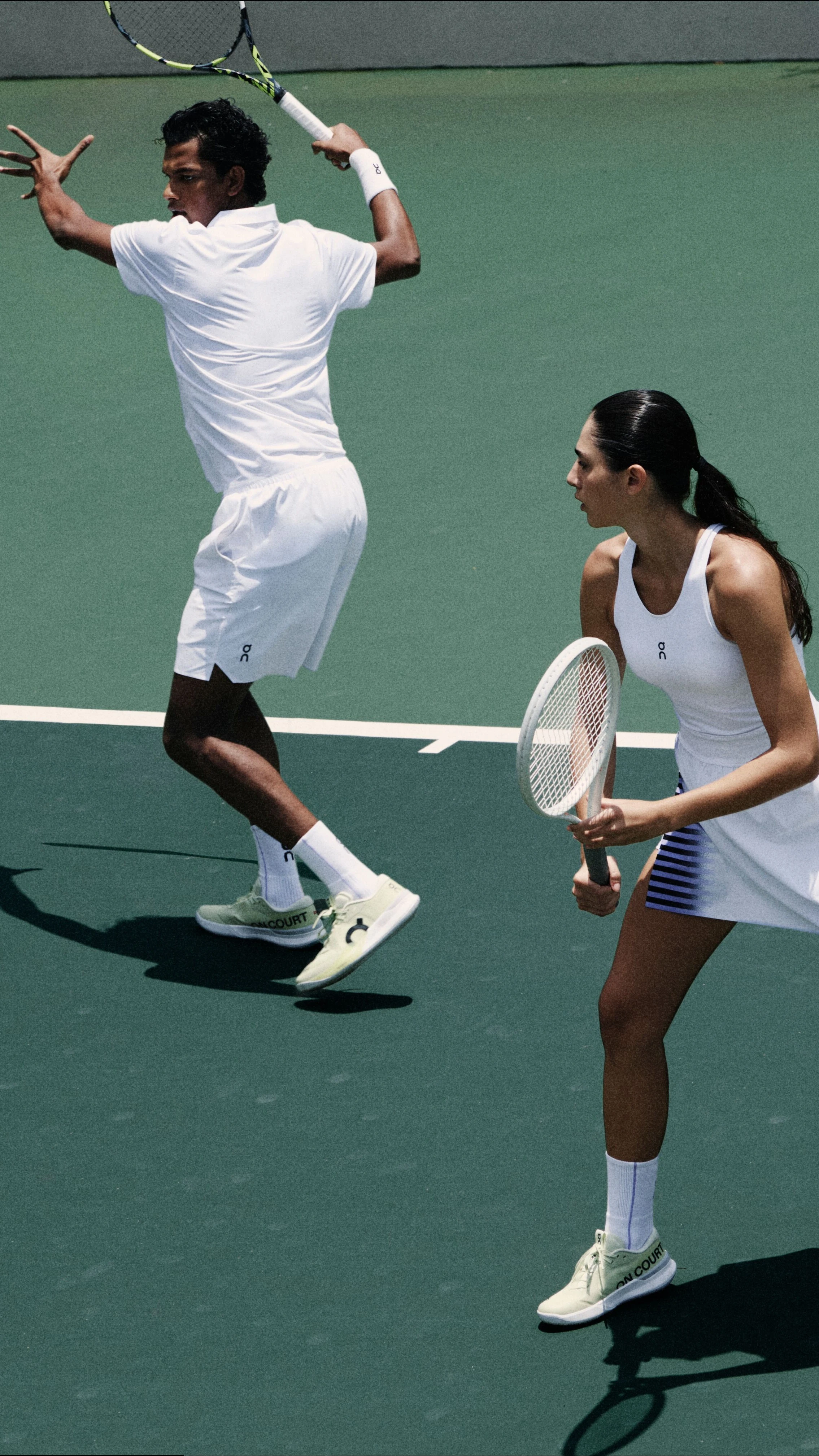 Tennis players in On tennis whites, mid swing.