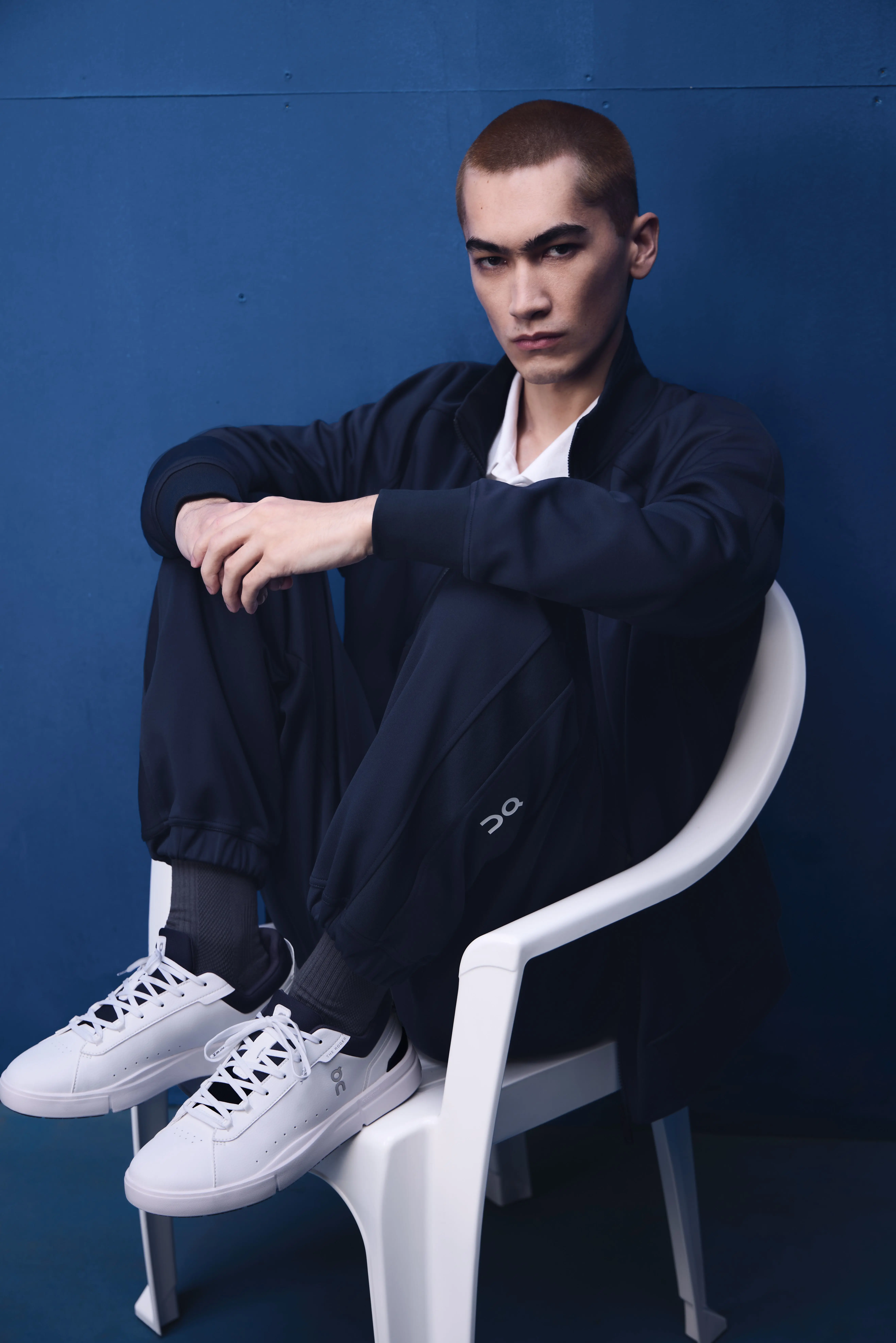 An athlete sitting on a lawn chair, knees to chest, showing their On sneakers.