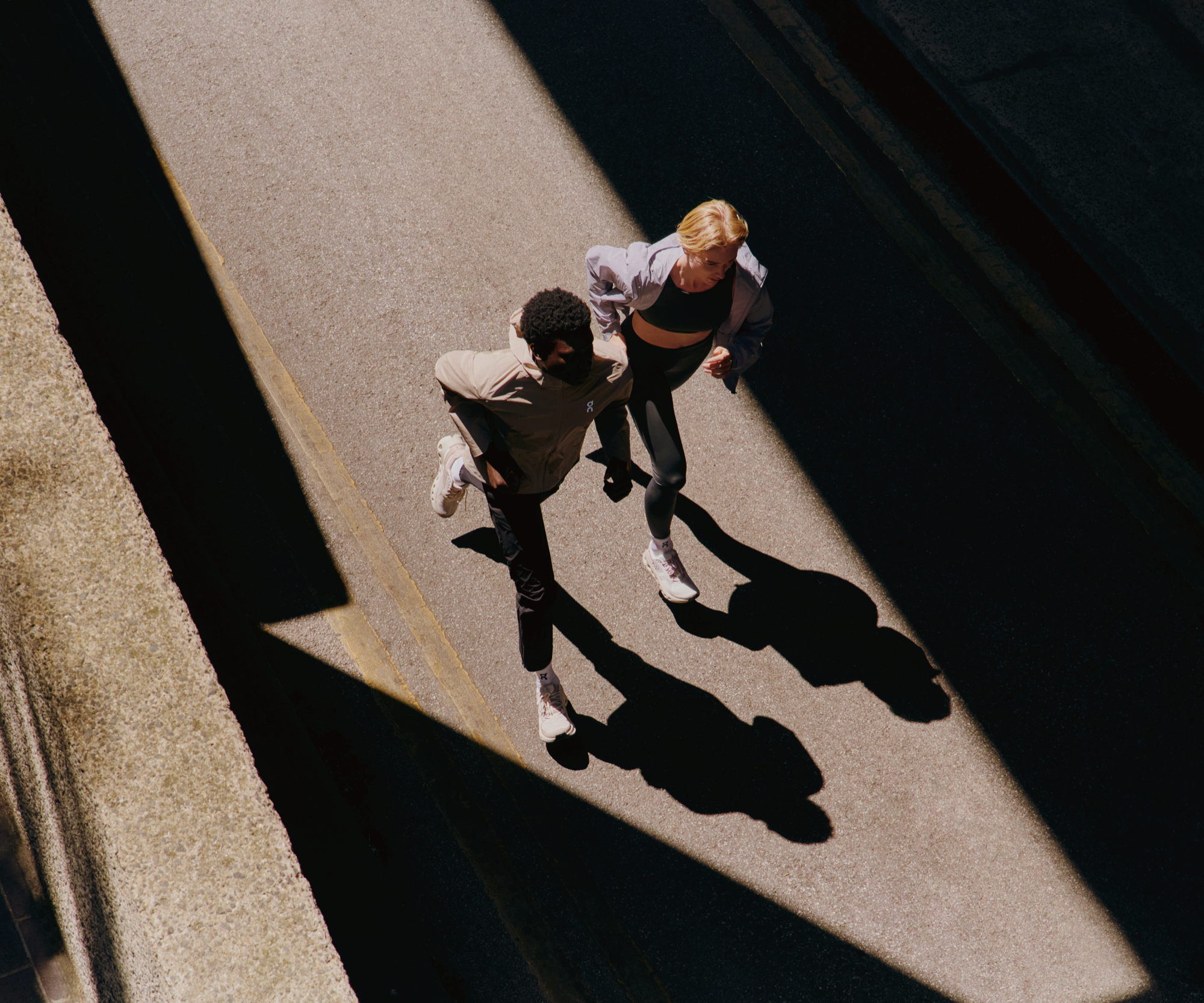 Two runners jogging on the street, wearing On performance hoodies and training shoes.