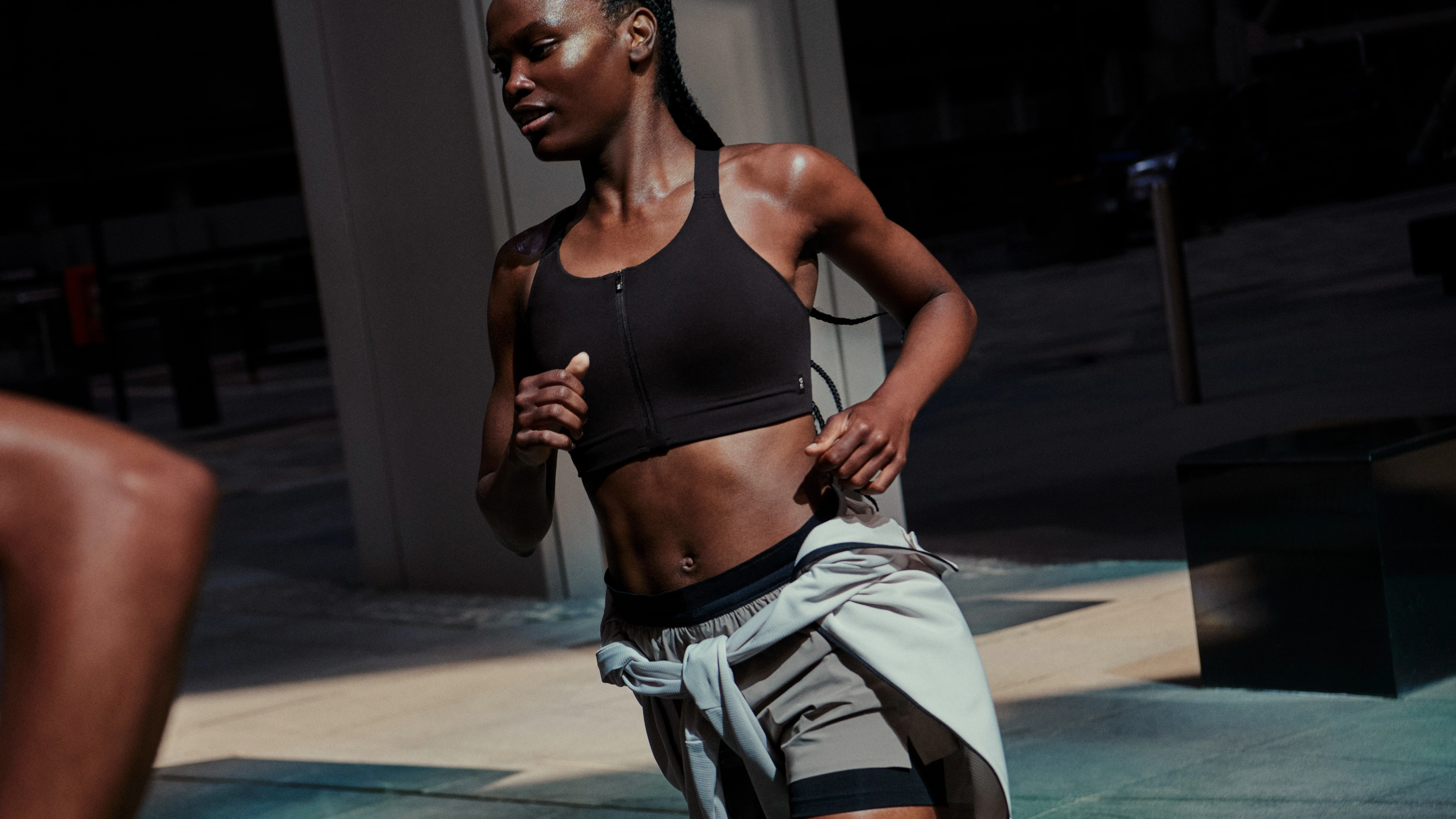 A runner running on pavement in a sports bra and shorts, with a sweater wrapped around their waist.