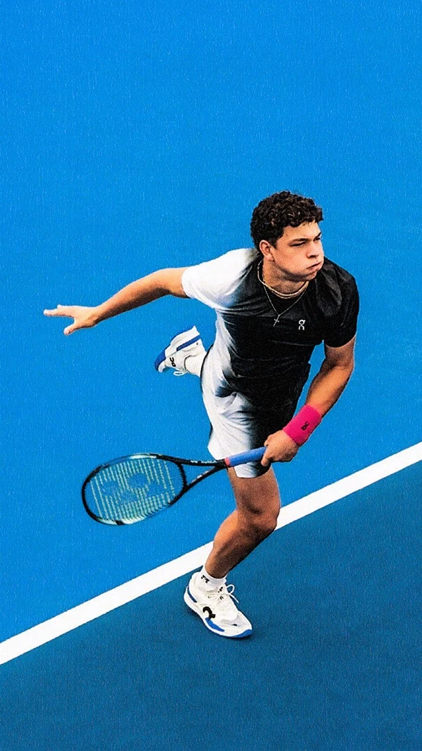Ben Shelton stands on a blue tennis court wearing On clothing.