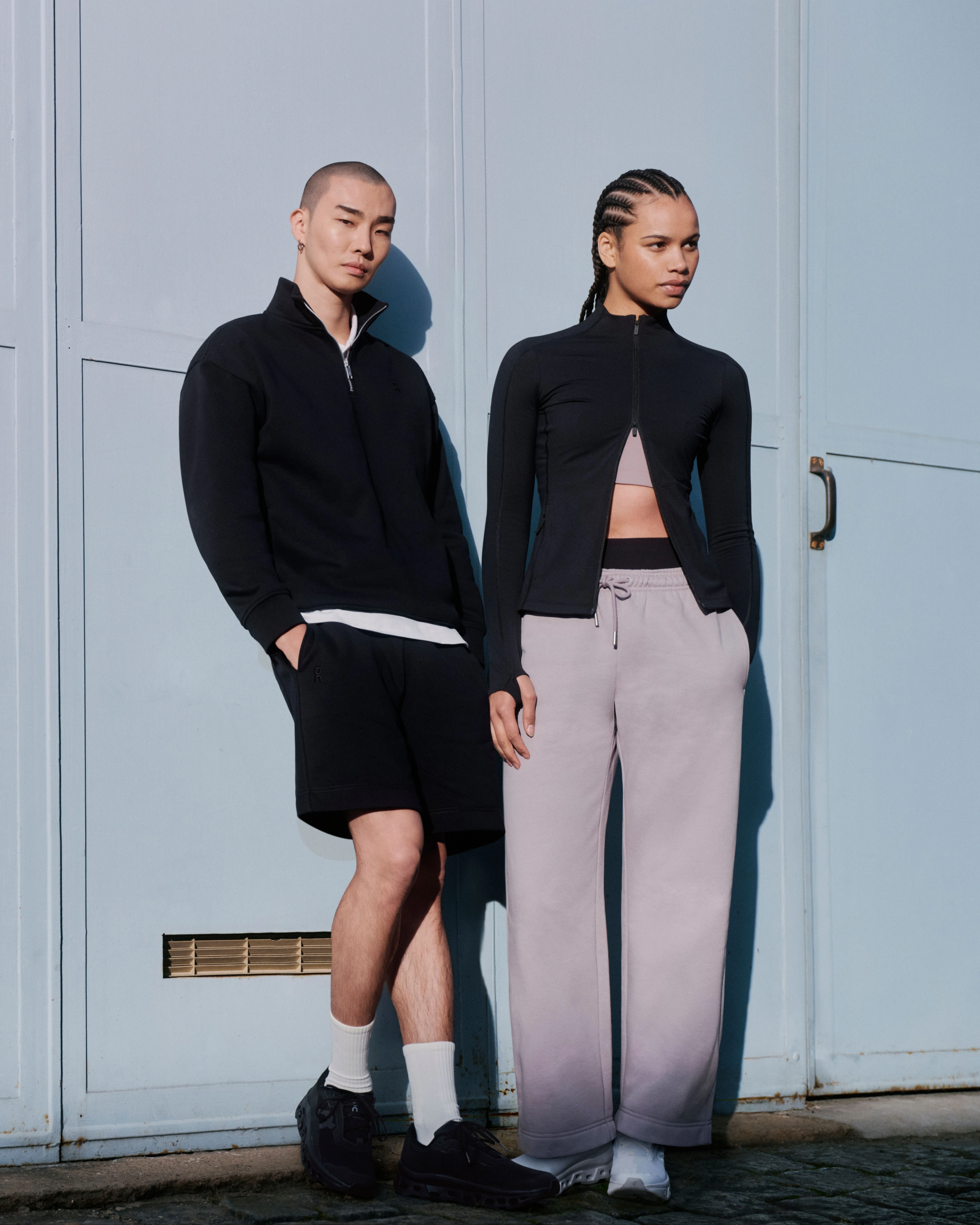 Two people in On streetwear, posing against a wall.