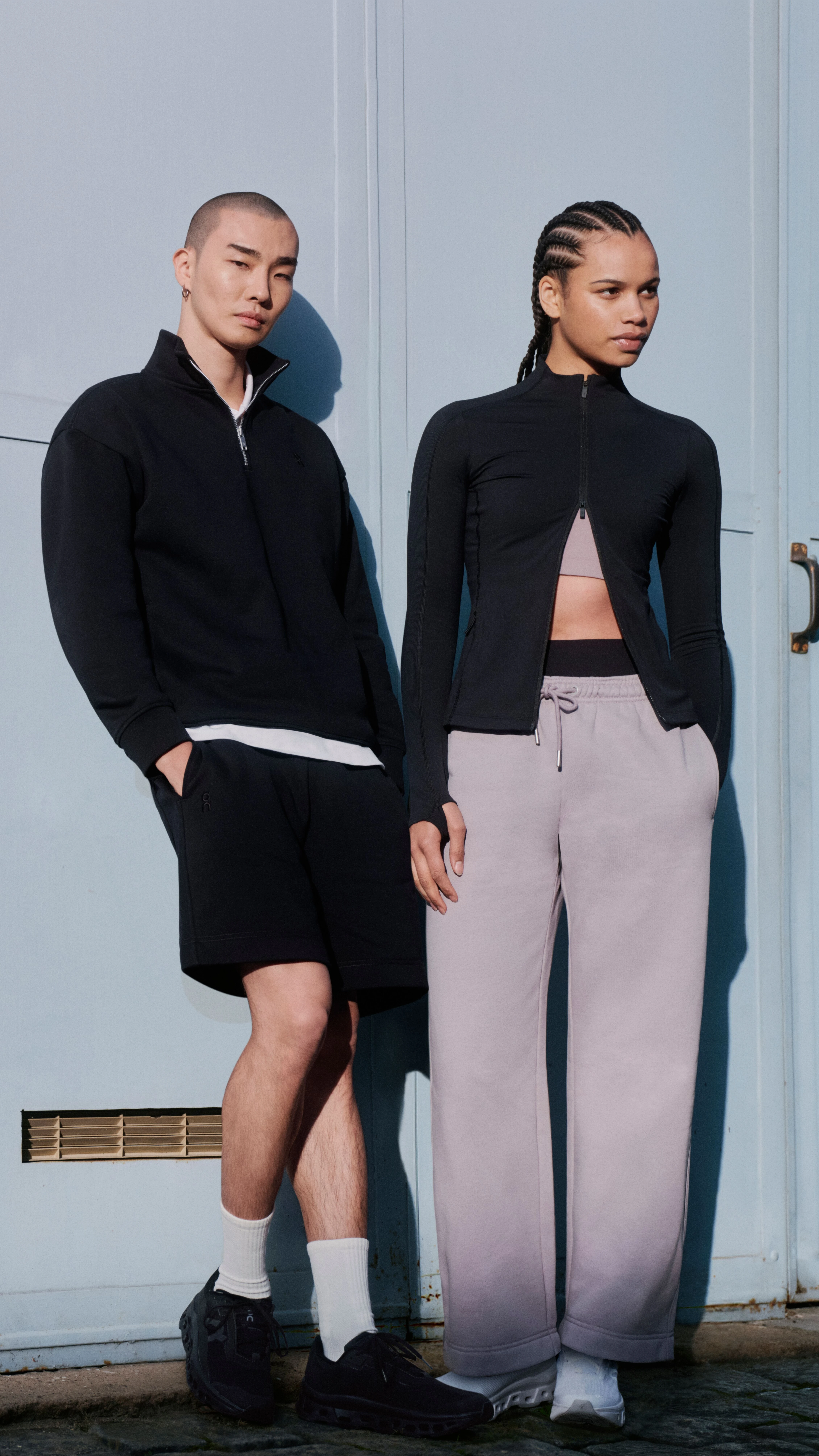 Two people in On streetwear, posing against a wall.