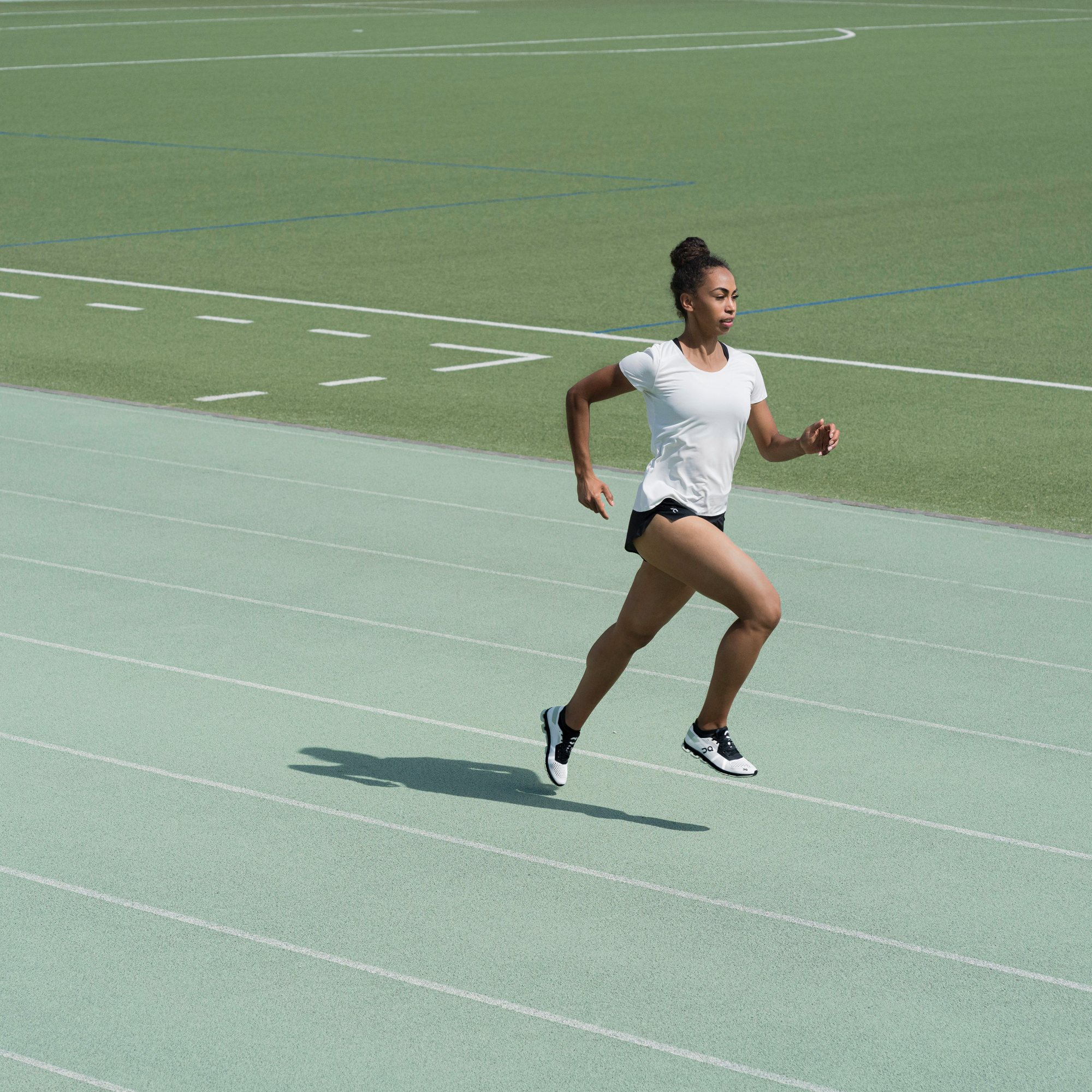 Woman running on a green track with football field in the background