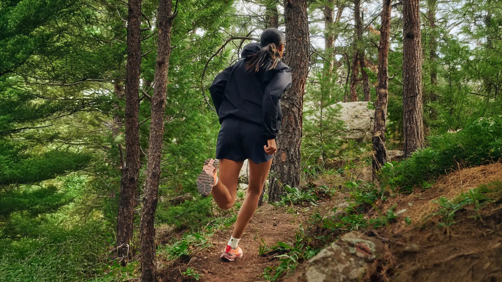 A woman runs through a forest trail.