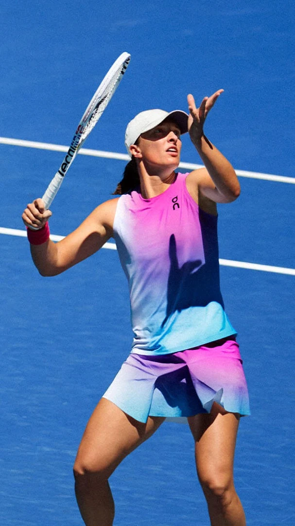 Iga Świątek tennis player in multi-colored clothing tosses a ball into the air.